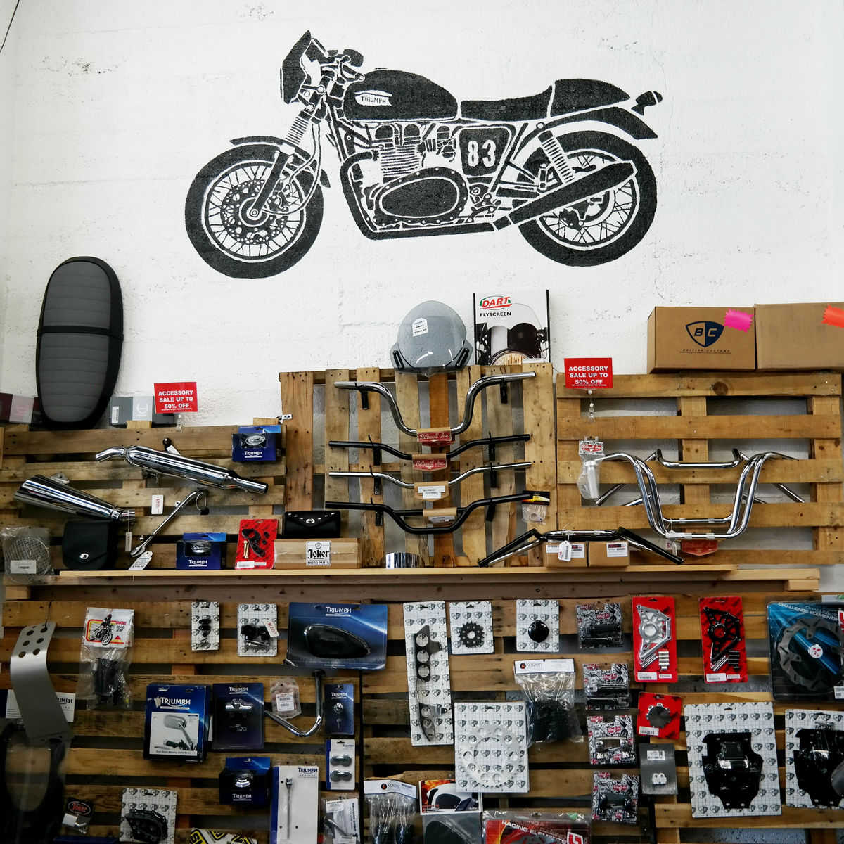Handlebars, gears, and other components attached to wall-mounted wooden pallets in the Triumph of …